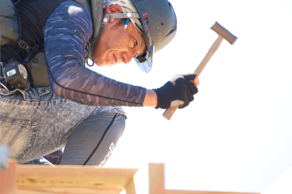 お家の骨組みの上でトンカチを握る大工さん