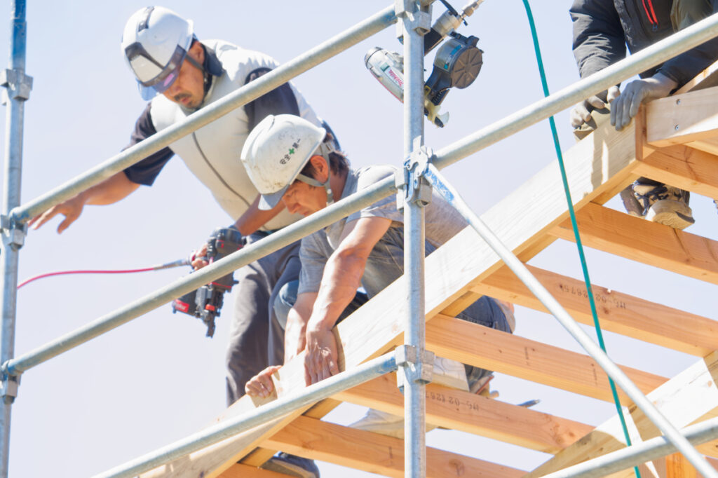 お家の骨組みの上で話し合う大工さん